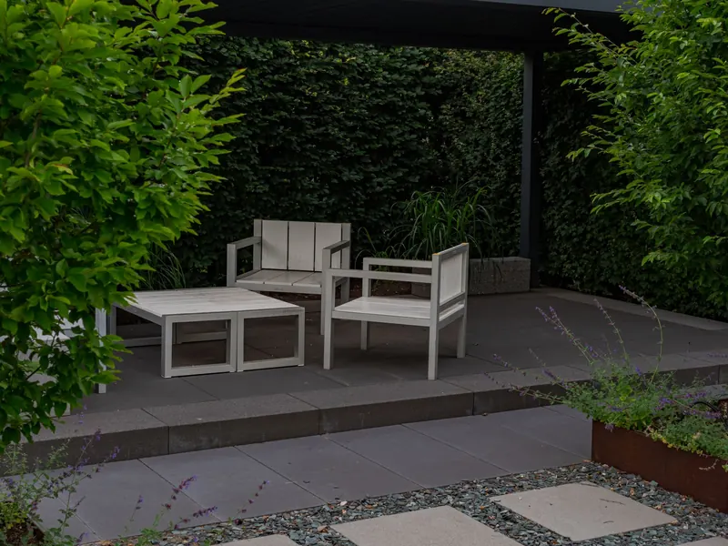 A serene outdoor patio featuring minimalist wooden furniture in a lush garden setting