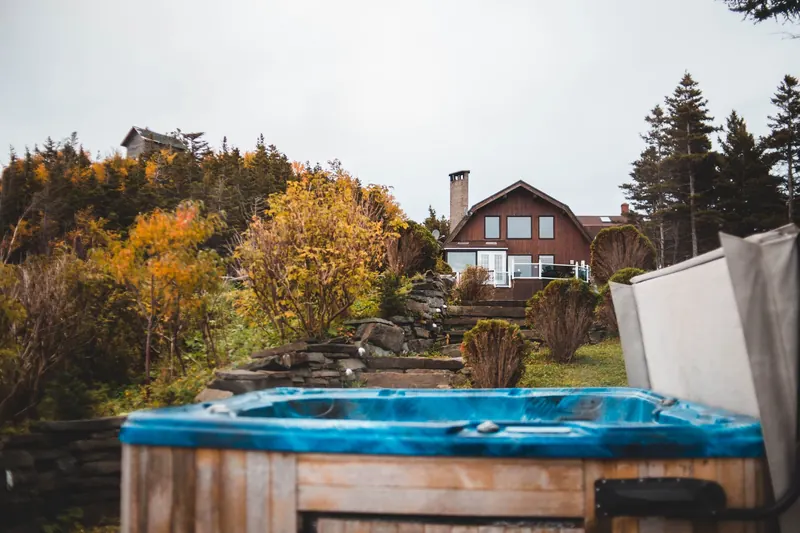 A serene countryside house surrounded by autumn foliage with a hot tub in the foreground