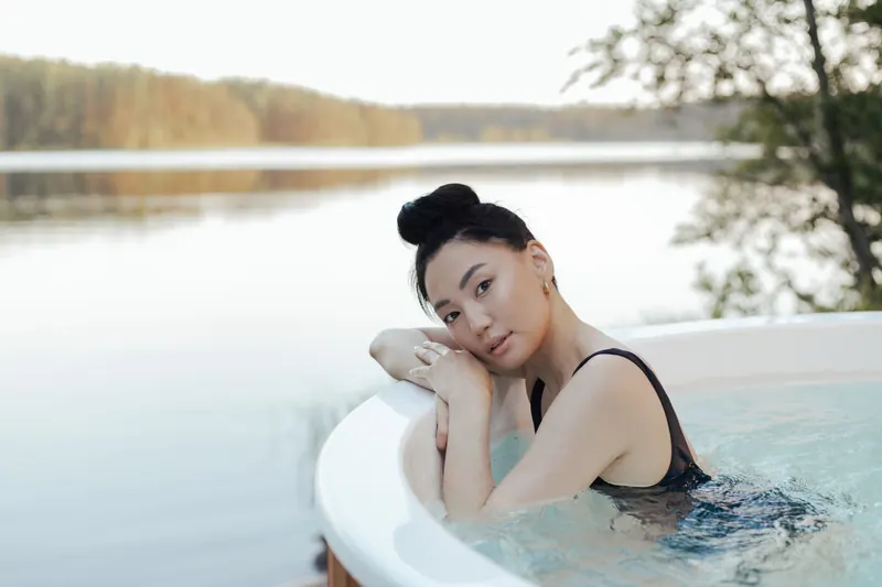 A woman enjoys a relaxing time in an outdoor hot tub by a serene lakeside setting